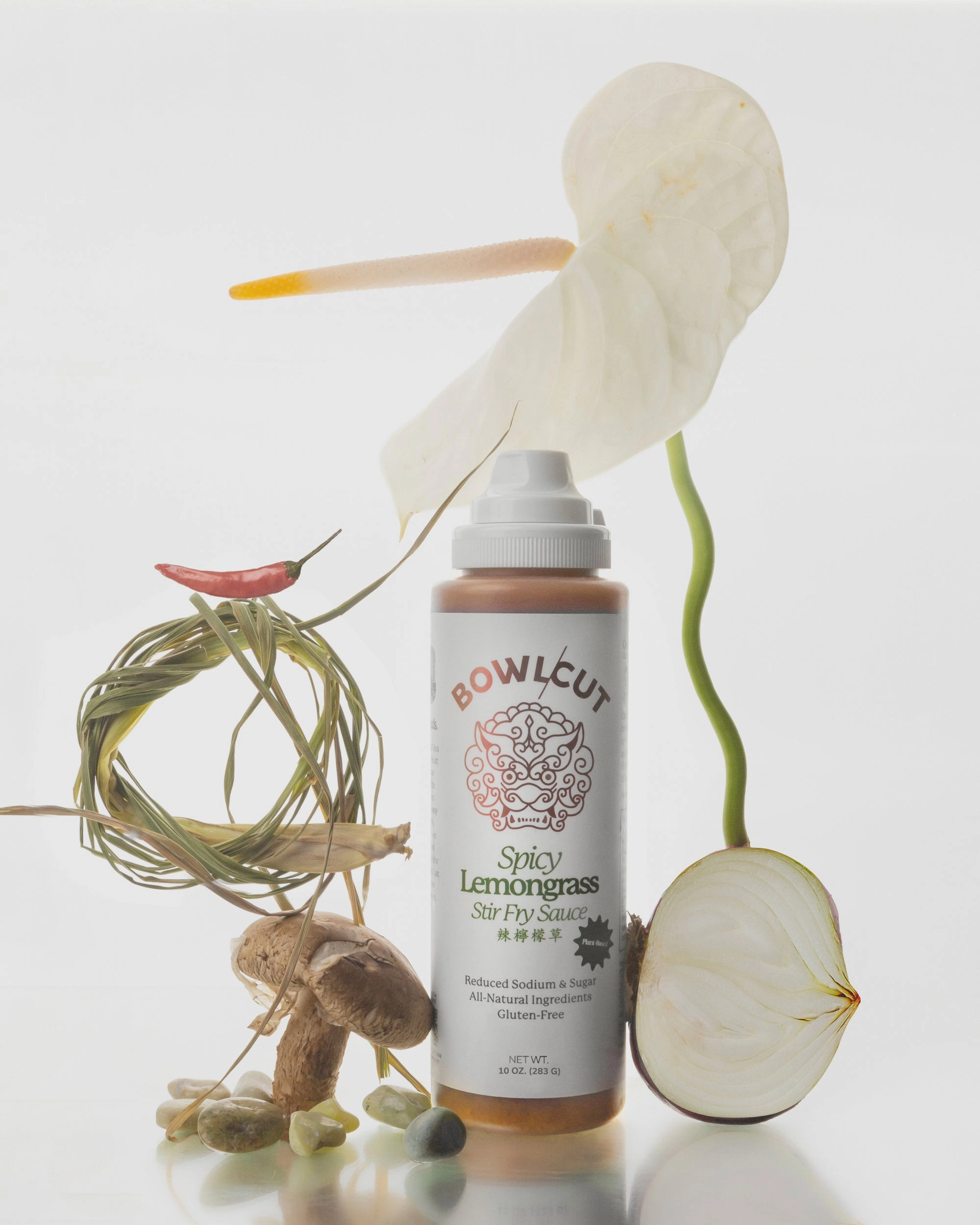Spicy Lemongrass Stir Fry Sauce bottle beside an anthurium, lemongrass and mushrooms