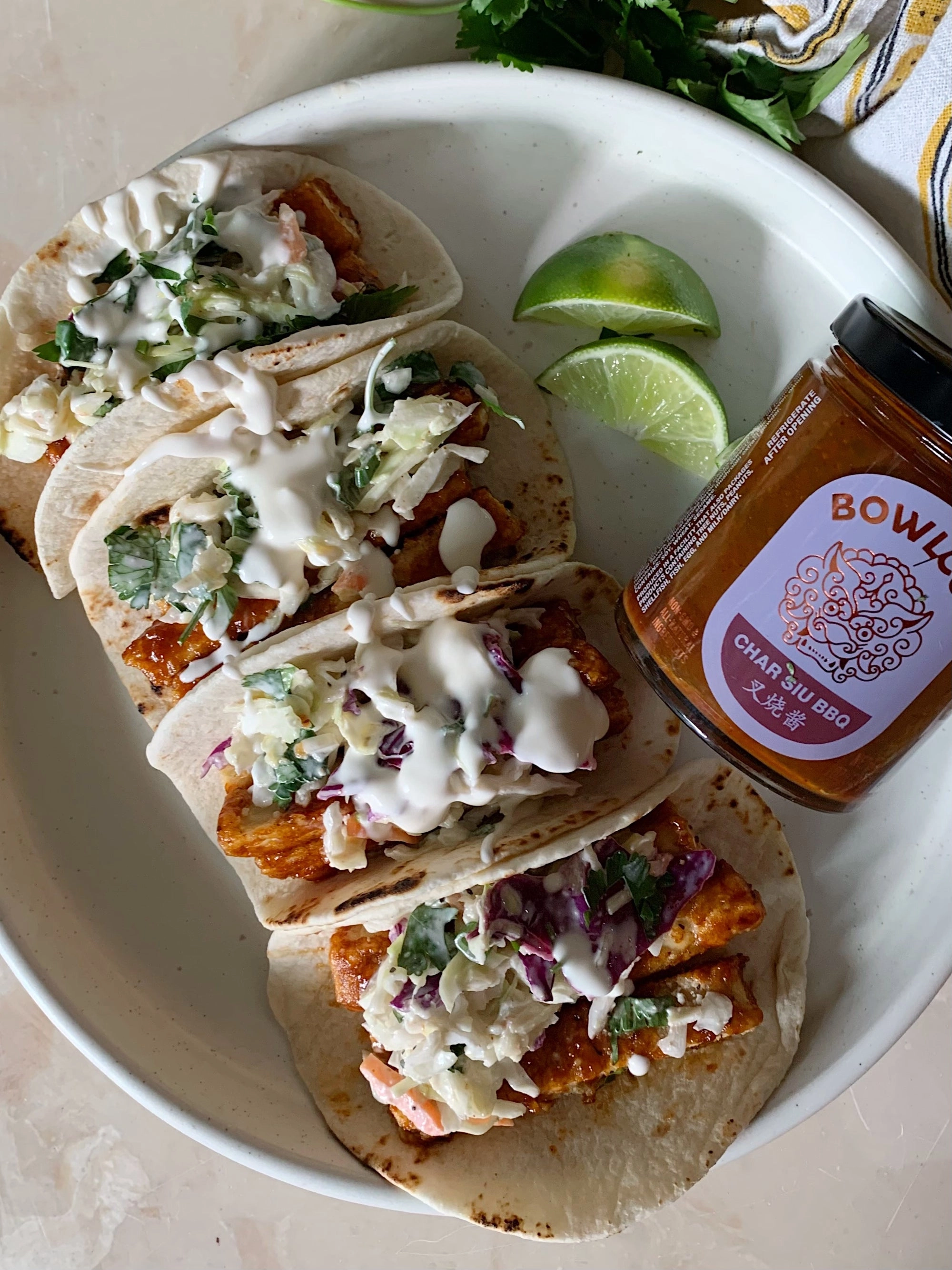 Tacos with slaw and lime beside a jar of Bowlcut sauce